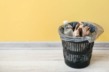 Sarı duvarın yanında farklı çöp kutuları olan plastik çöp kutusu.