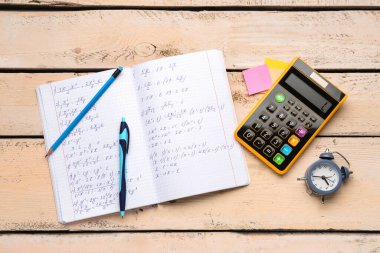Matematik formülleri, hesap makinesi, alarm saati ve bej ahşap zemin üzerine kırtasiye defteri