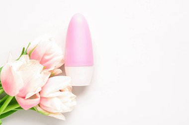 Deodorant şişesi ve beyaz arka planda çiçekler.