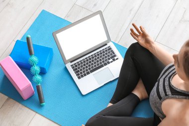 Dizüstü bilgisayarlı genç bir kadın spor salonunda yoga yapıyor.