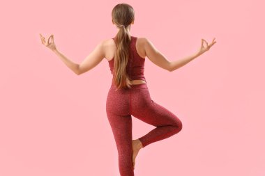 Pembe arka planda yoga yapan genç bir kadın.
