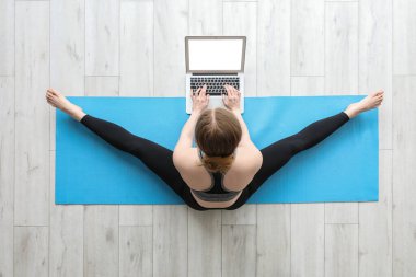 Dizüstü bilgisayarlı genç bir kadın spor salonunda yoga yapıyor.