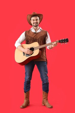 Kırmızı arka planda gitar çalan yakışıklı kovboy.