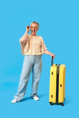 Mavi arka planda bavulu olan olgun bir kadın.