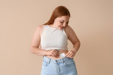 Bej arka plana doğum kontrol bandı yapıştıran genç bir kadın.