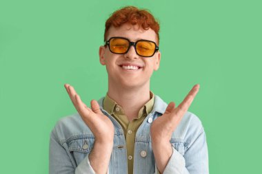 Yeşil arka planda güneş gözlüklü genç kızıl adam.