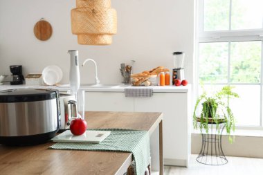 Mutfaktaki ahşap masada blender, tost makinesi, çoklu fırın ve elma.