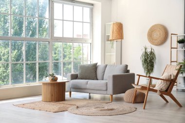 Gri kanepeli, sehpalı, koltuklu ve büyük pencereli aydınlık oturma odasının içi.