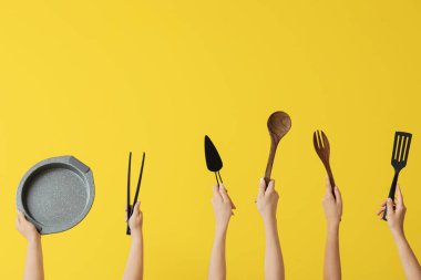 Sarı arka planda pişirme aletleri olan kadın eller.