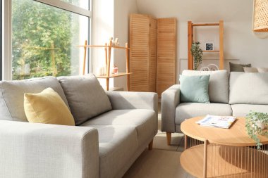 Işıl ışıl oturma odasının içi rahat gri koltuklar ve ahşap kahve masası.