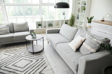 Işıl ışıl oturma odasının içi rahat gri koltuklar, kahve masası ve büyük pencereli.