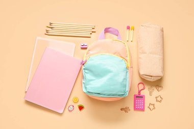 Turuncu arka planda farklı kırtasiye malzemesi olan şık bir okul çantası.