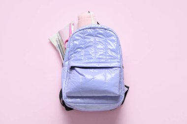 Pembe arka planda kırtasiye malzemesi olan leylak rengi okul çantası