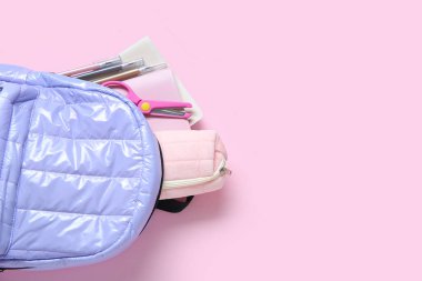 Pembe arka planda kırtasiye malzemesi olan leylak rengi okul çantası