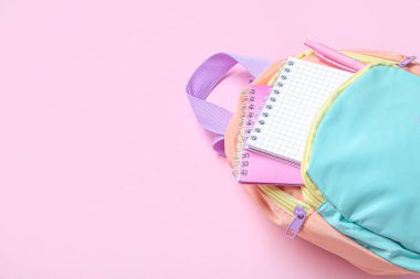 Pembe arka planda kırtasiye malzemesi olan renkli okul çantası