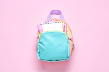 Pembe arka planda kırtasiye malzemesi olan renkli okul çantası