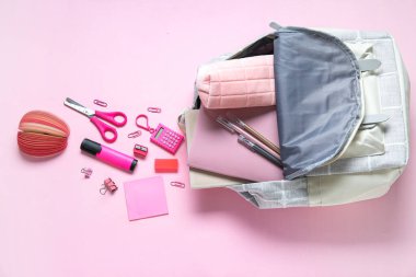 Pembe arka planda farklı kırtasiye malzemesi olan renkli okul çantası