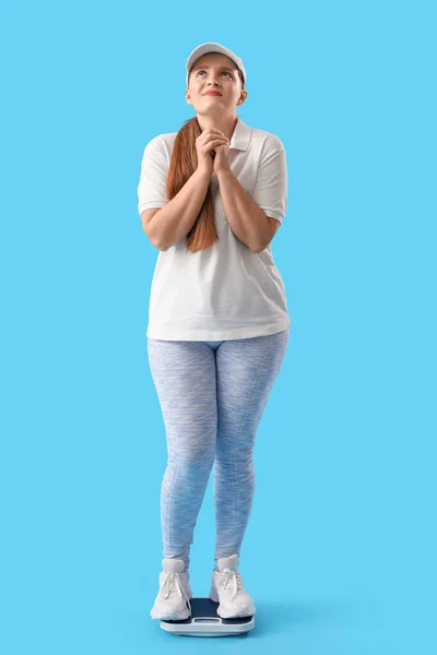 Беспокойная Молодая Женщина Измеряет Свой Вес Весах Синем Фоне — стоковое фото