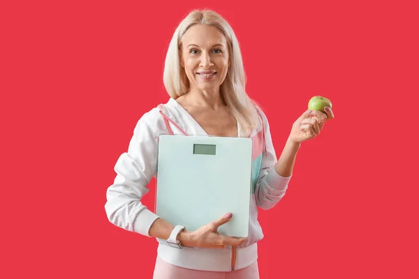 Sportliche Reife Frau Mit Schuppen Und Apfel Auf Rotem Hintergrund — Stockfoto