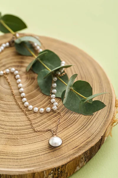 緑の背景に真珠のネックレスとユーカリの枝と木製のスタンド クローズアップ — ストック写真