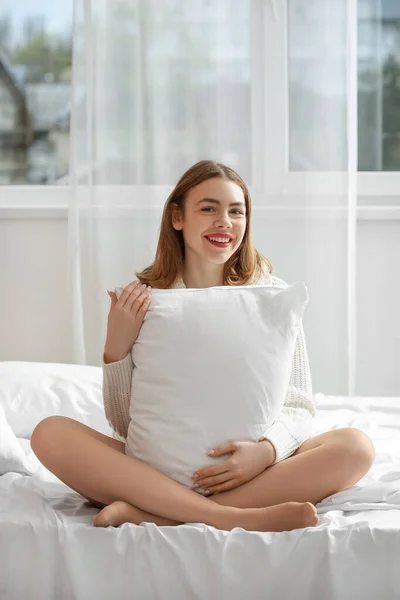 ベージュタイツとベッドに座っている枕で美しい若い女性 — ストック写真