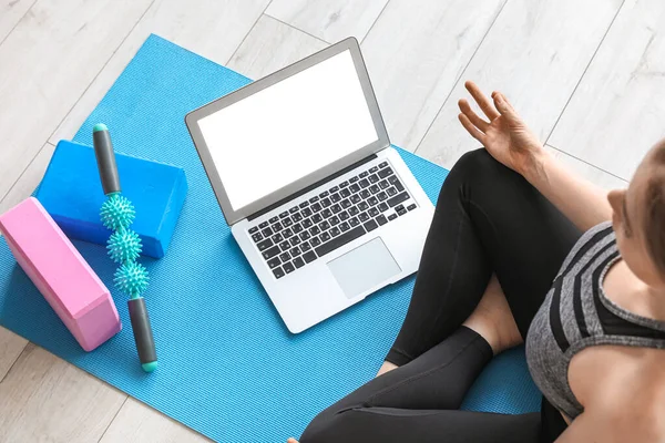 Sporty young woman with laptop doing yoga in gym