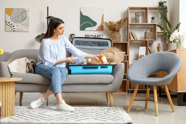 stock image Young woman packing sunscreen cream in suitcase at home