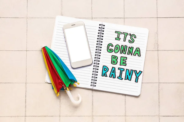 笔记本的文字 它的要去是Rainy 手机和伞白色的瓷砖背景 天气预报概念 — 图库照片