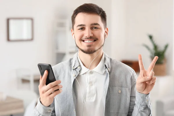 Jovem Com Telefone Celular Fones Ouvido Mostrando Gesto Vitória Casa — Fotografia de Stock