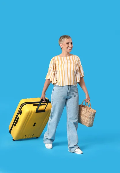 stock image Mature woman with suitcase and bag walking on blue background