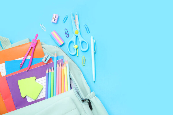 Зеленый рюкзак школы с различными канцелярскими принадлежностями на синем фоне