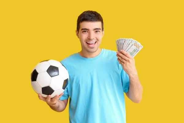 黄色の背景にサッカーボールとお金を持っている幸せな若者 スポーツベットコンセプト — ストック写真