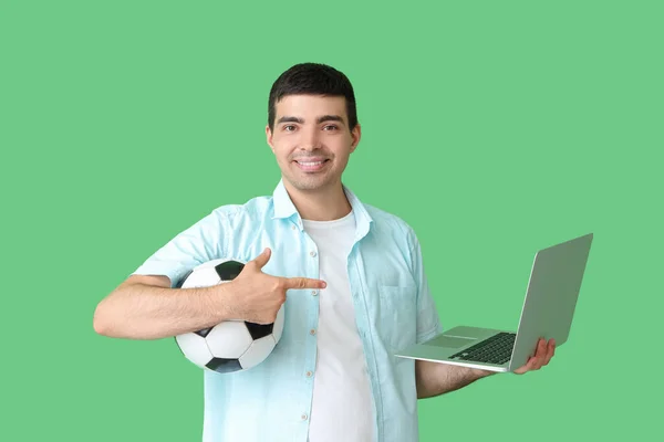 サッカーボールを持った若者は 緑色の背景にノートパソコンを指差します スポーツベットコンセプト — ストック写真