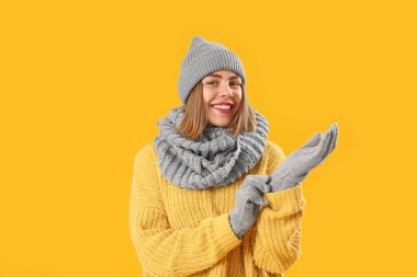 Frozen young woman in winter clothes on yellow background