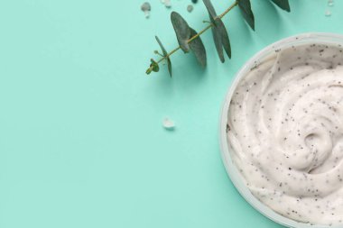 Jar of body scrub and eucalyptus branch on color background