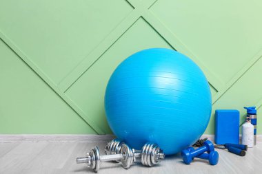 Spor aletleri spor salonunda yeşil duvarın yanında dambıllı.