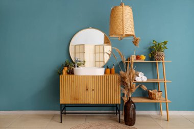 Beyaz lavabo ve banyo aksesuarları çekmecelerin, lambaların ve çiçeklerin olduğu odada renk duvarının yanında.