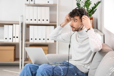 Kanepede dizüstü bilgisayarlı erkek teknik destek ajanı oturuyor.