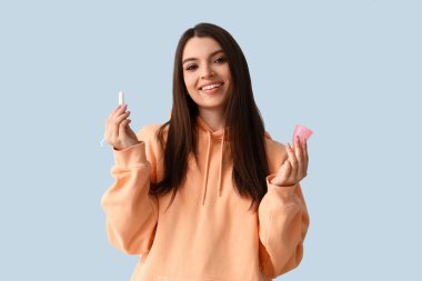 Mavi arka planda tampon ve regl bardağı olan genç bir kadın.