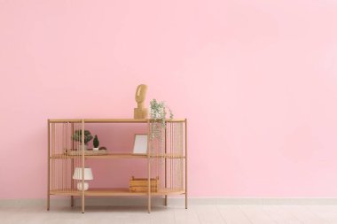 Odada pembe duvarın yanında çiçek ve dekor bulunan modern raf ünitesi.