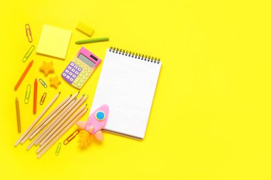 Plastikten yapılmış roket ve sarı zemin üzerinde kırtasiye malzemesi olan boş bir defter.