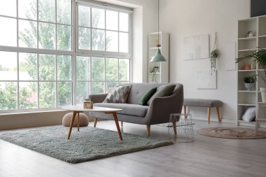 Gri kanepeli, kahve masalı ve büyük pencereli aydınlık oturma odasının içi.