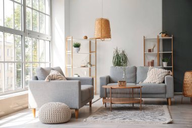 Gri koltukları, kahve masası ve geniş pencereli aydınlık oturma odasının içi.