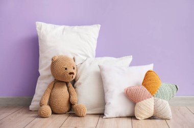 Leylak duvarının yanında oyuncak ayı olan beyaz yastıklar.