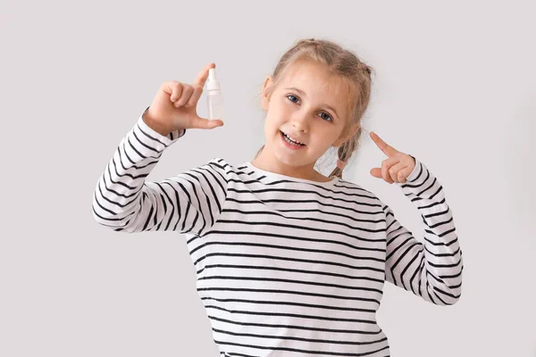 Little girl pointing at eye drops on light background