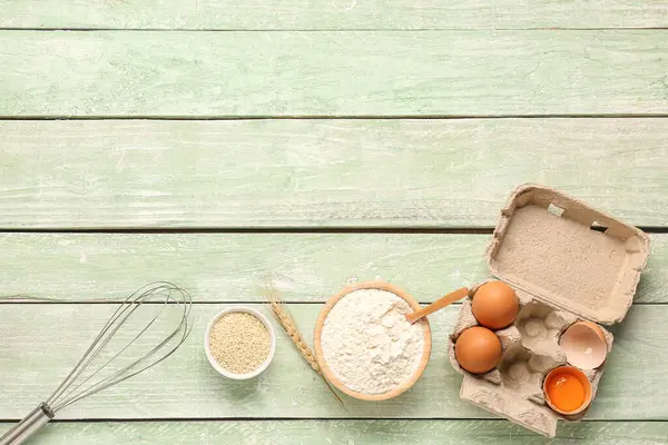 stock image Composition with bowl of wheat flour, sesame seeds, eggs and whisk on green wooden table