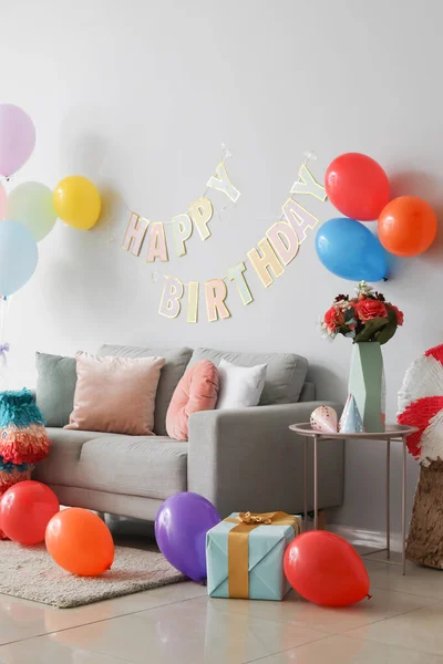 Interior of living room decorated for birthday with balloons, gift box and garland