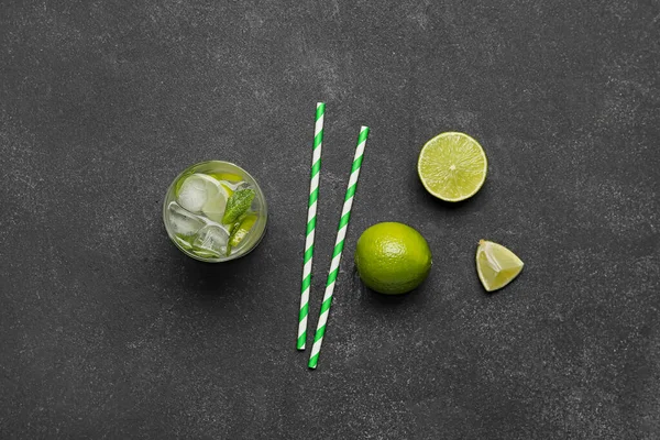 stock image Glass of tasty mojito, fresh fruits and straws on dark background