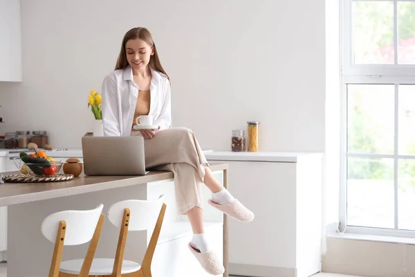 Щаслива Молода Жінка Тримає Чашку Кави Сидить Столі Сучасним Ноутбуком — стокове фото