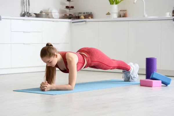 瘦小的年轻女子在轻便厨房的瑜伽垫上运动 — 图库照片